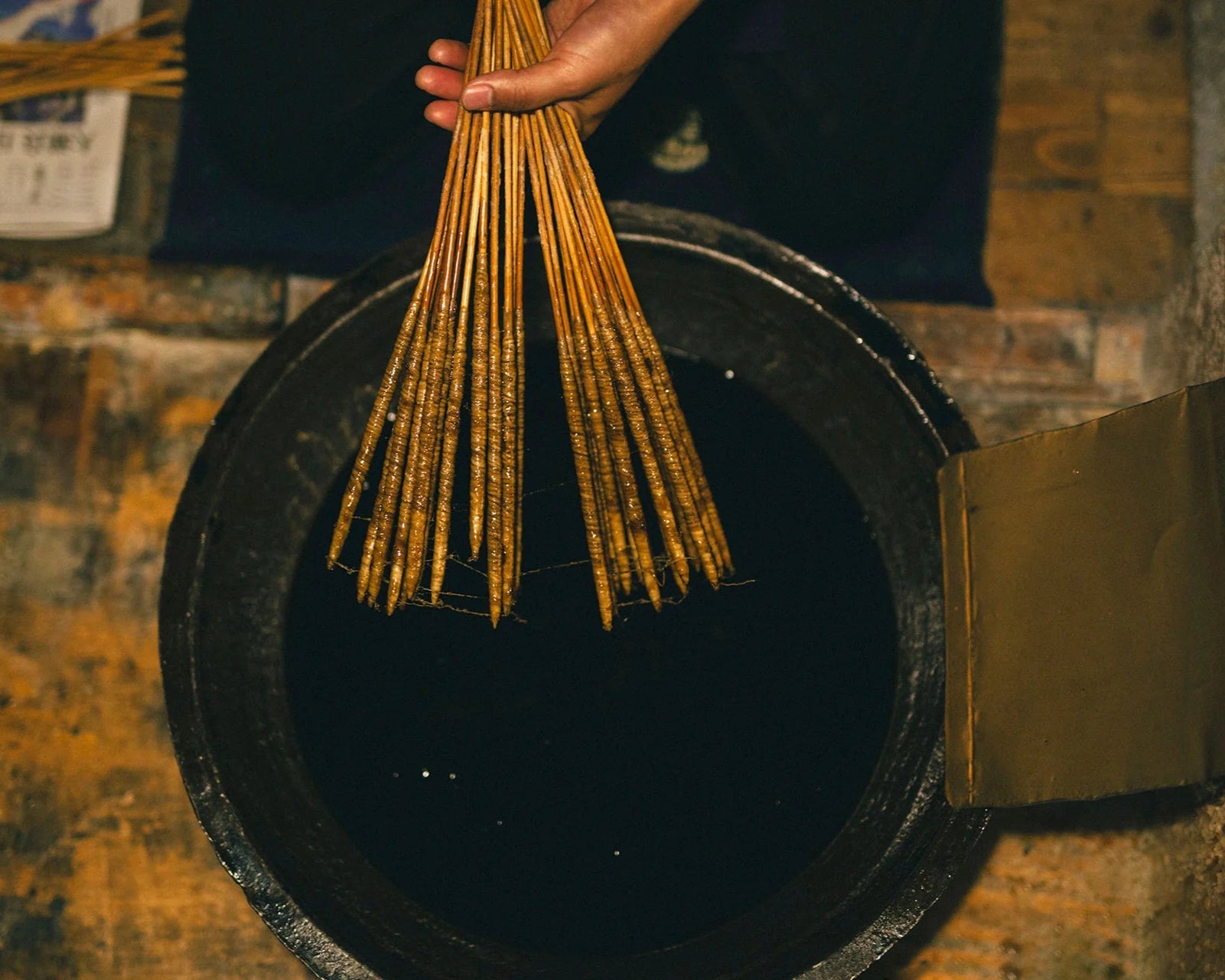 Hand holding incense sticks over a black container on a textured surface