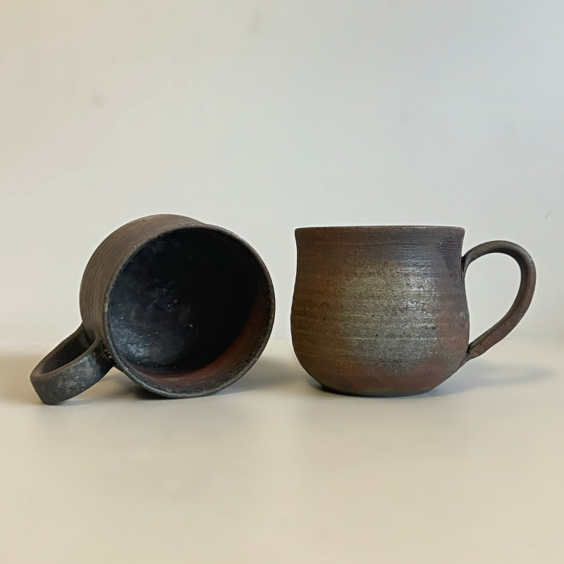 A rustic, handcrafted ceramic mug with a round shape and an earthy, textured surface, featuring shades of brown and gray, made by Tsugaru Kanayama pottery in Japan.