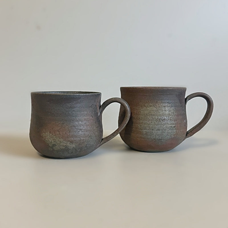 A rustic, handcrafted ceramic mug with a round shape and an earthy, textured surface, featuring shades of brown and gray, made by Tsugaru Kanayama pottery in Japan.